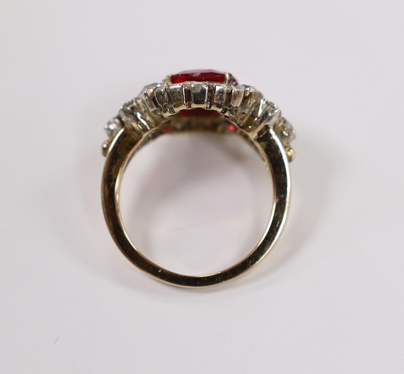 A yellow metal, singe stone round cut synthetic ruby and diamond set circular cluster dress ring, with diamond set shoulders, size J/K, gross weight 4.3 grams.